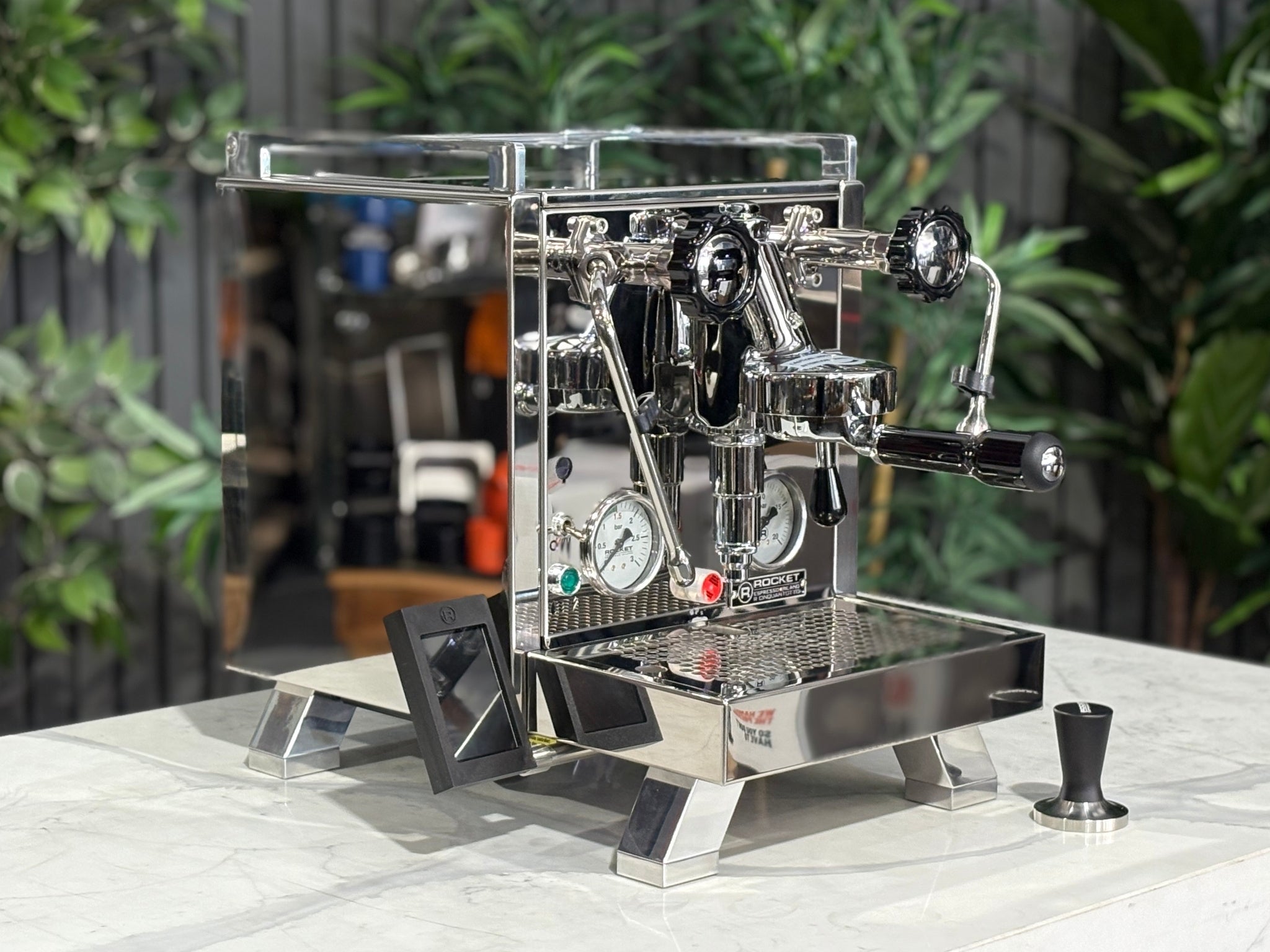 Rocket Cinquantotto R58 1 Group Coffee Machine Stainless - New angled view showing the polished stainless steel body, E61 group head, cool touch steam wand, and wide drip tray on a marble bench with greenery in the background.