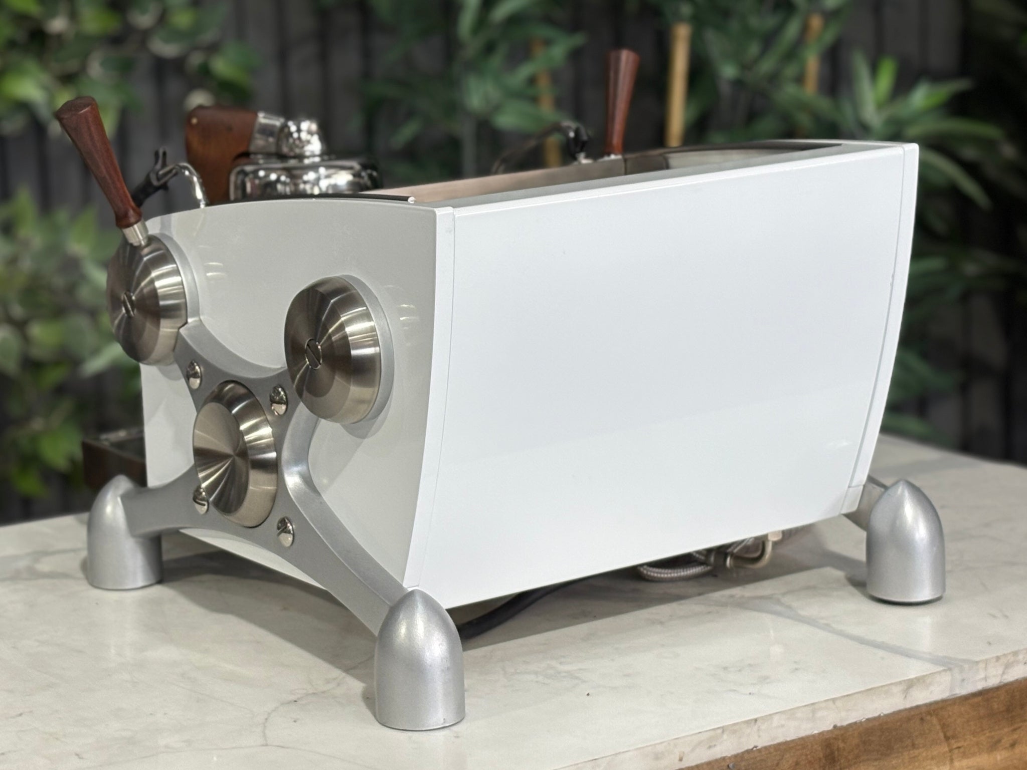 Slayer Espresso 1 Group Coffee Machine White – Used, angled back view showing the rear panel, side profile, and dual steam wands of the espresso coffee machine on a marble bench with greenery visible behind.