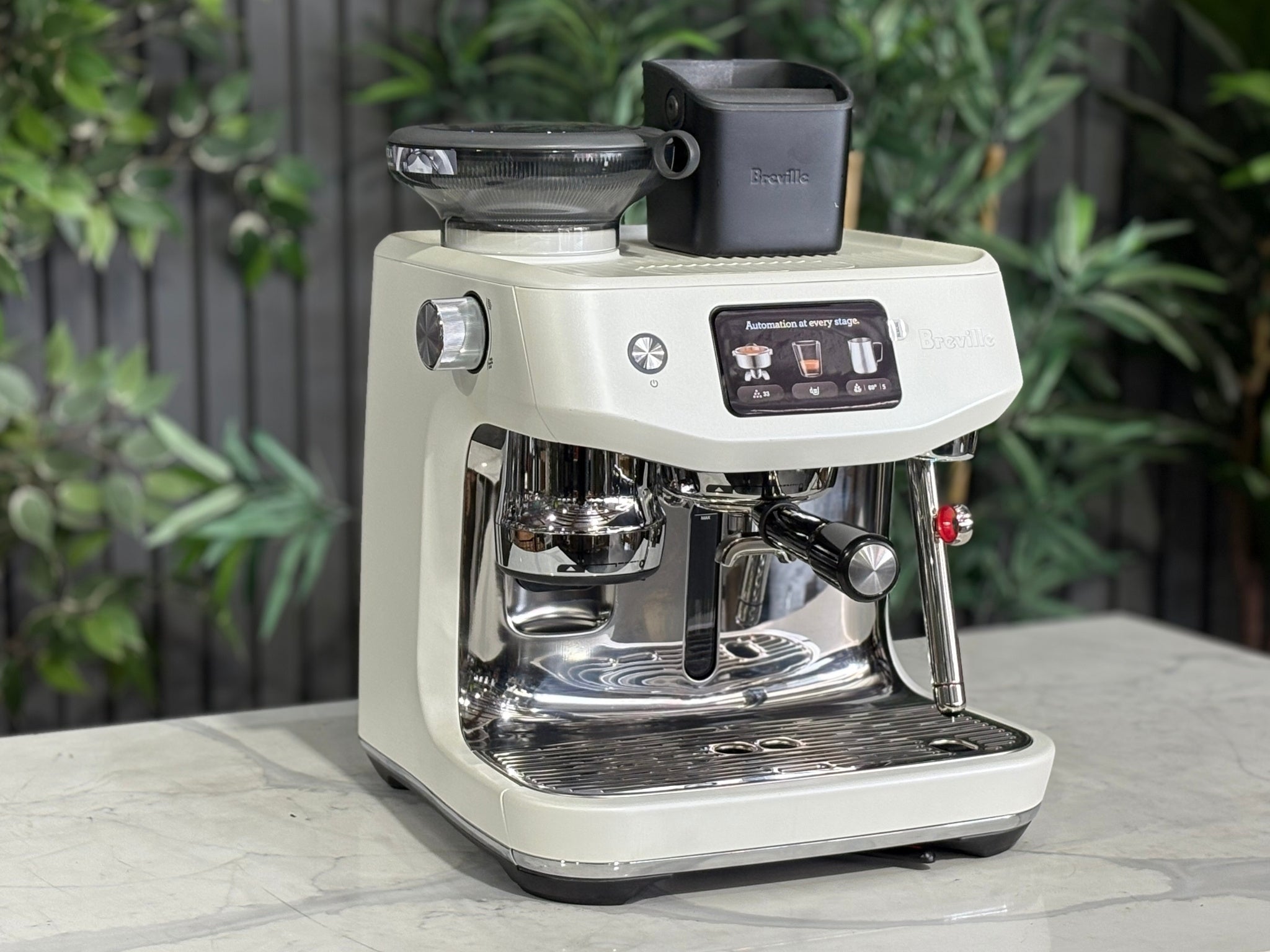 Breville Oracle Jet 1 Group Coffee Machine White - New, angled view on a marble bench with greenery, showing the white body, espresso group head, milk steamer, and 340g hopper.