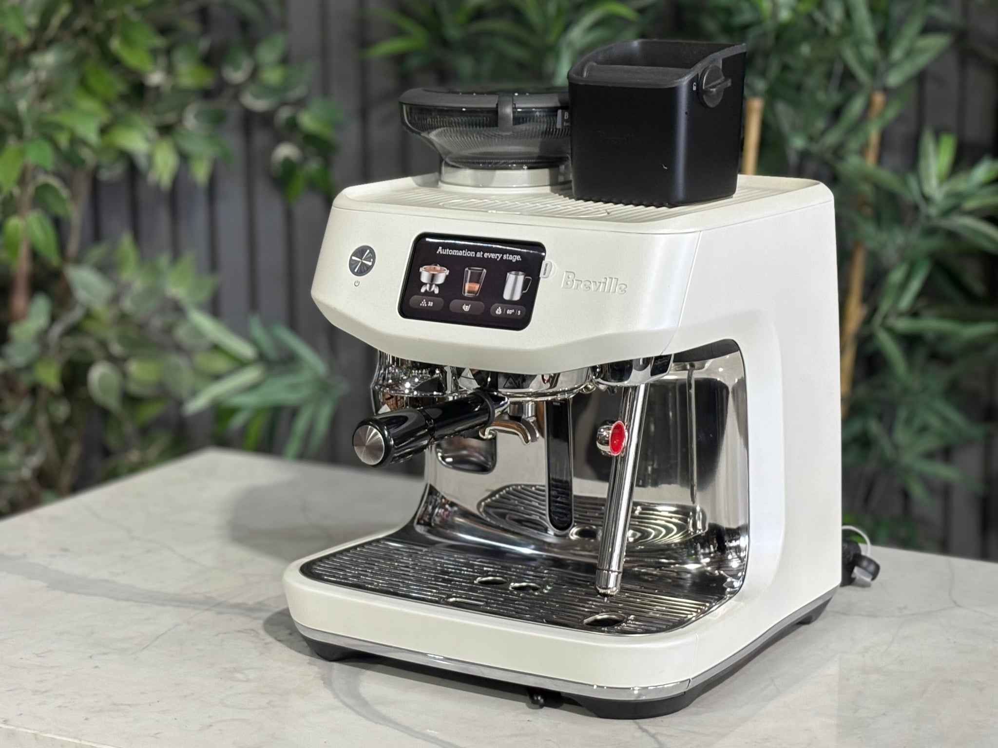 Breville Oracle Jet 1 Group Coffee Machine White - New, angled view on a marble bench with greenery, showing the white body, espresso group head, milk steamer, and 340g hopper.