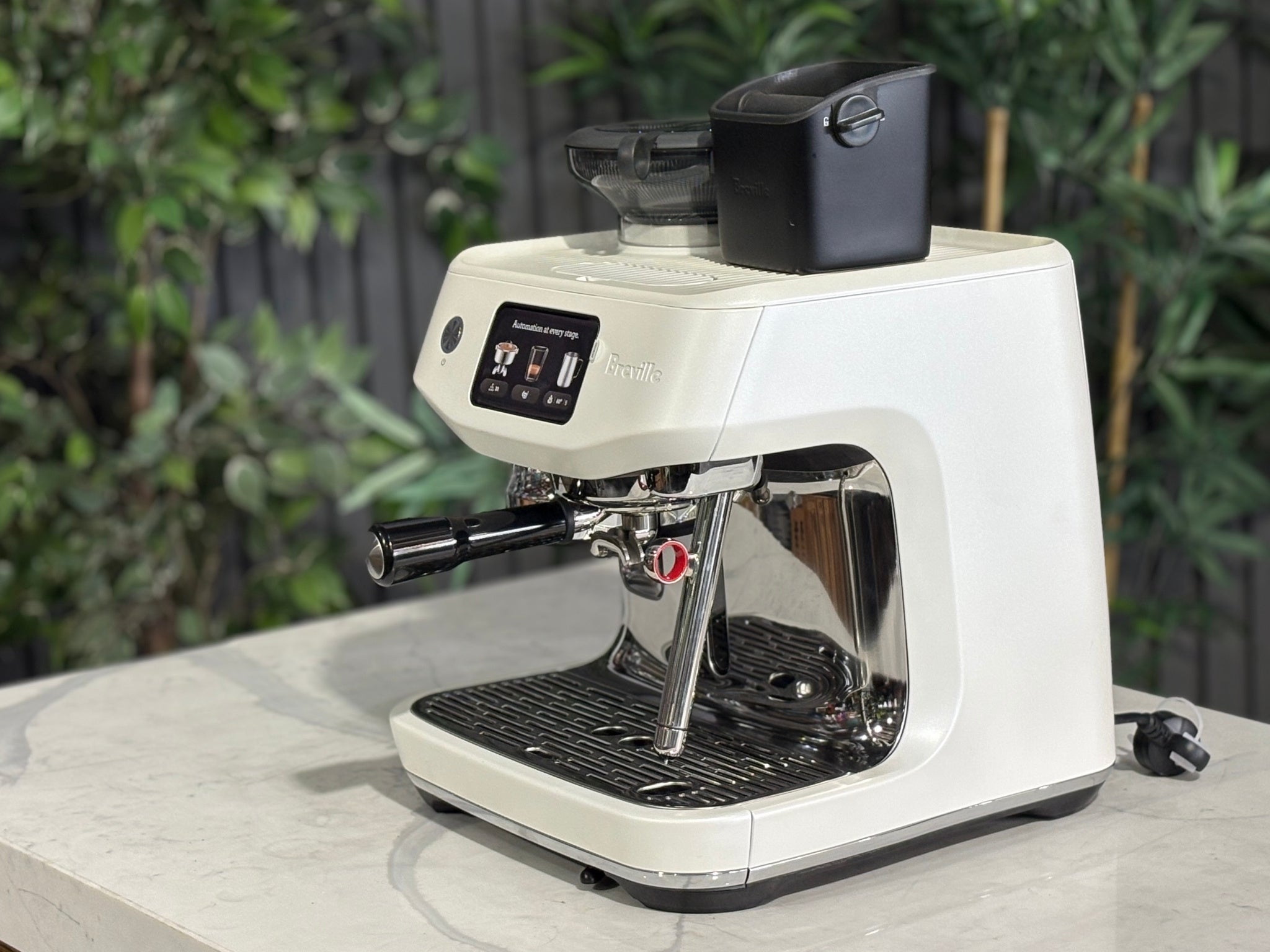 Breville Oracle Jet 1 Group Coffee Machine White - New, angled view on a marble bench with greenery, showing the white body, espresso group head, milk steamer, and 340g hopper.