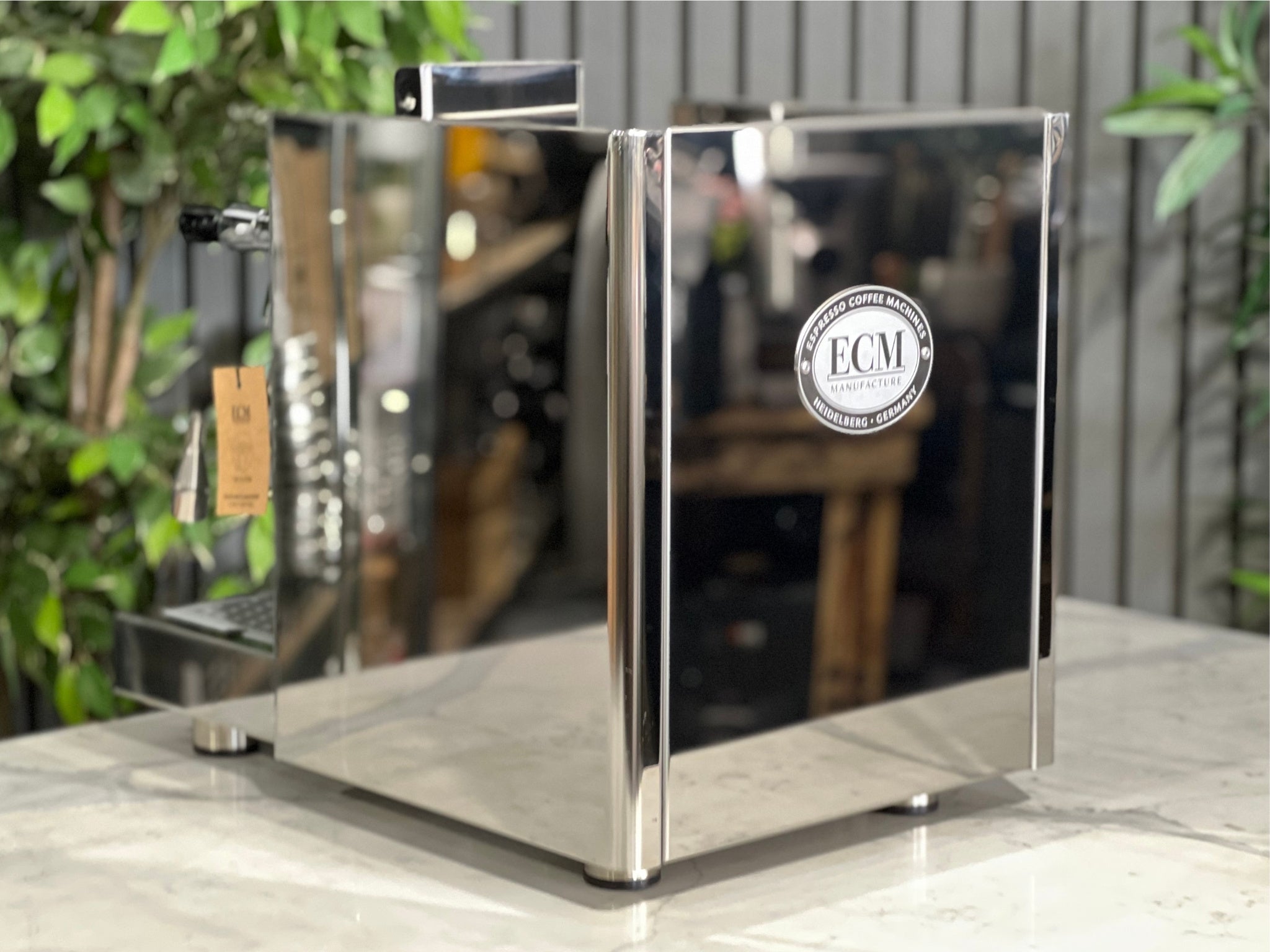 ECM Elektronika II Profi Rotary 1 Group Espresso Coffee Machine Stainless – New, angled rear view showing the stainless steel body and overall design on a marble bench with greenery behind.