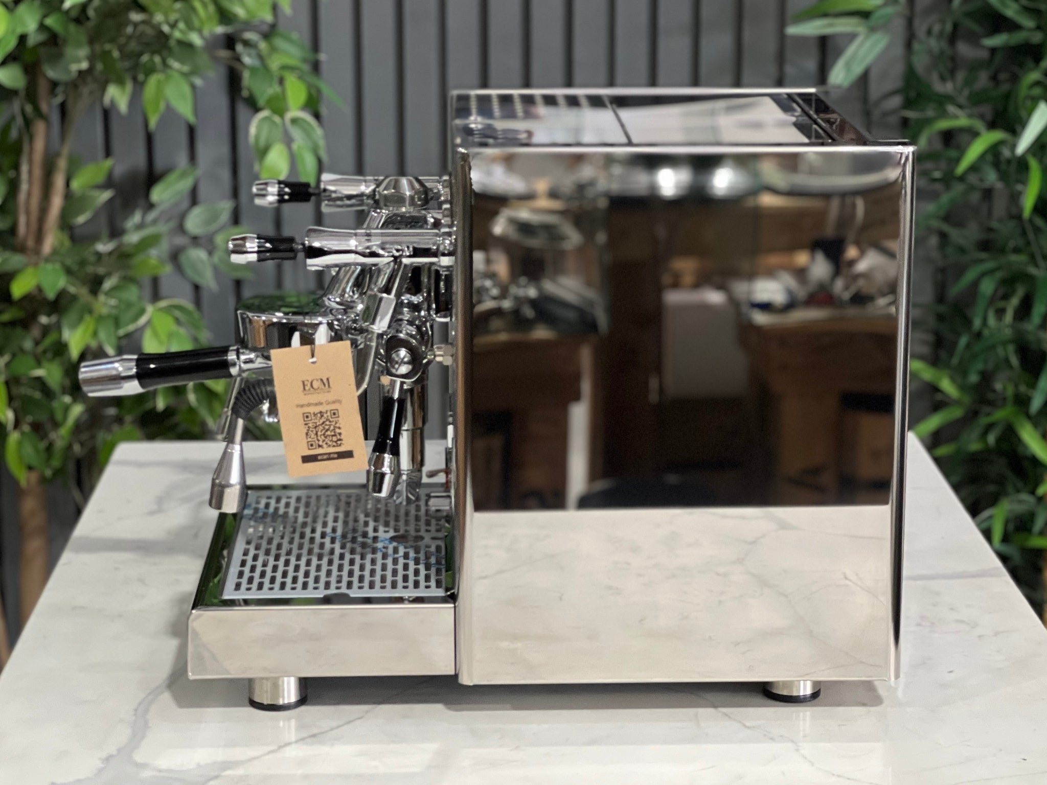 Side profile of the ECM Technika V Profi Rotary PID 1 Group Coffee Machine Stainless – New espresso coffee machine on a marble bench with greenery behind, highlighting the mirror-finish side panels, steam wand, and classic ECM design