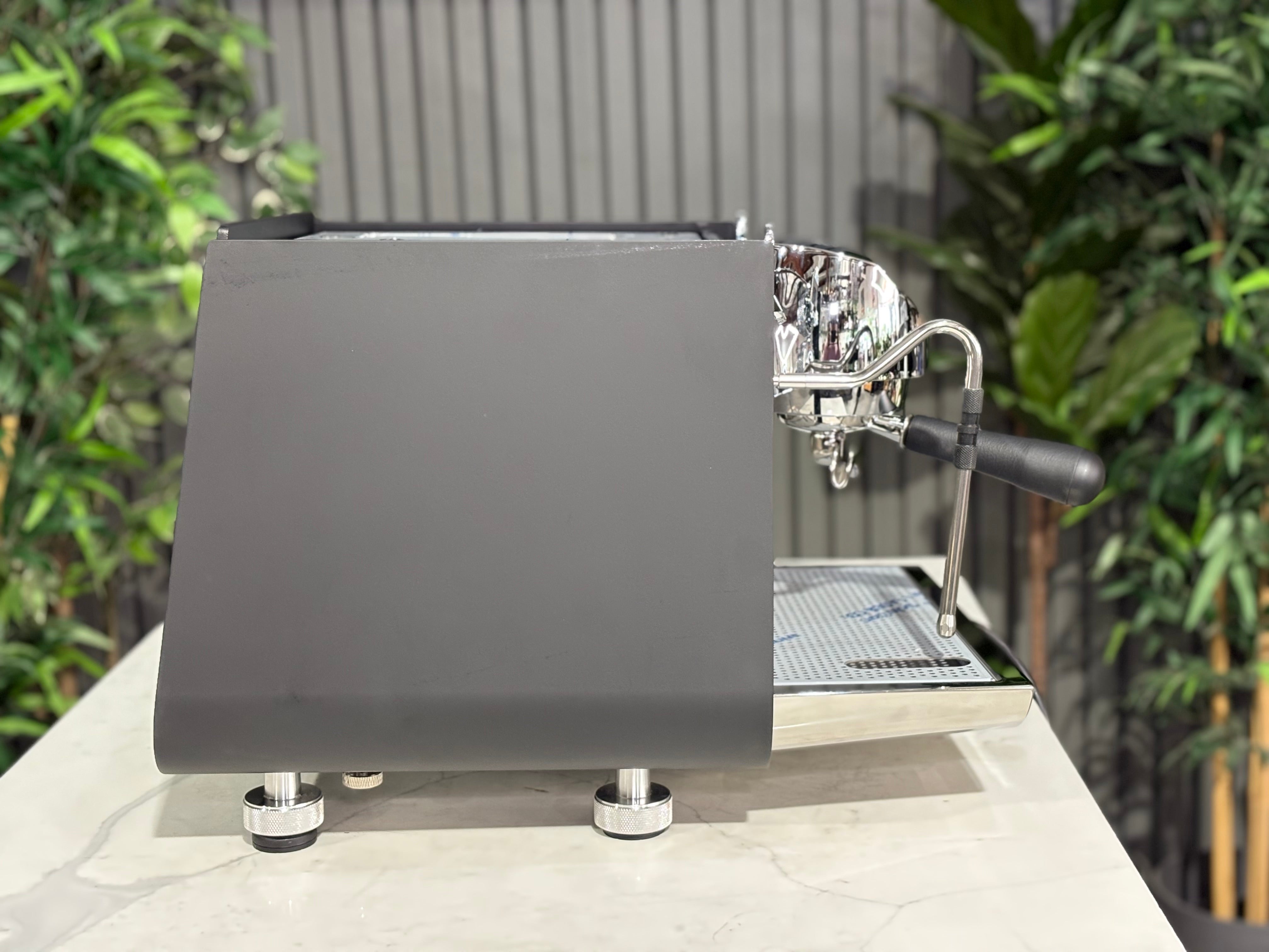 Victoria Arduino Eagle One Prima 1 Group Coffee Machine Black side view on a countertop with greenery in the background.