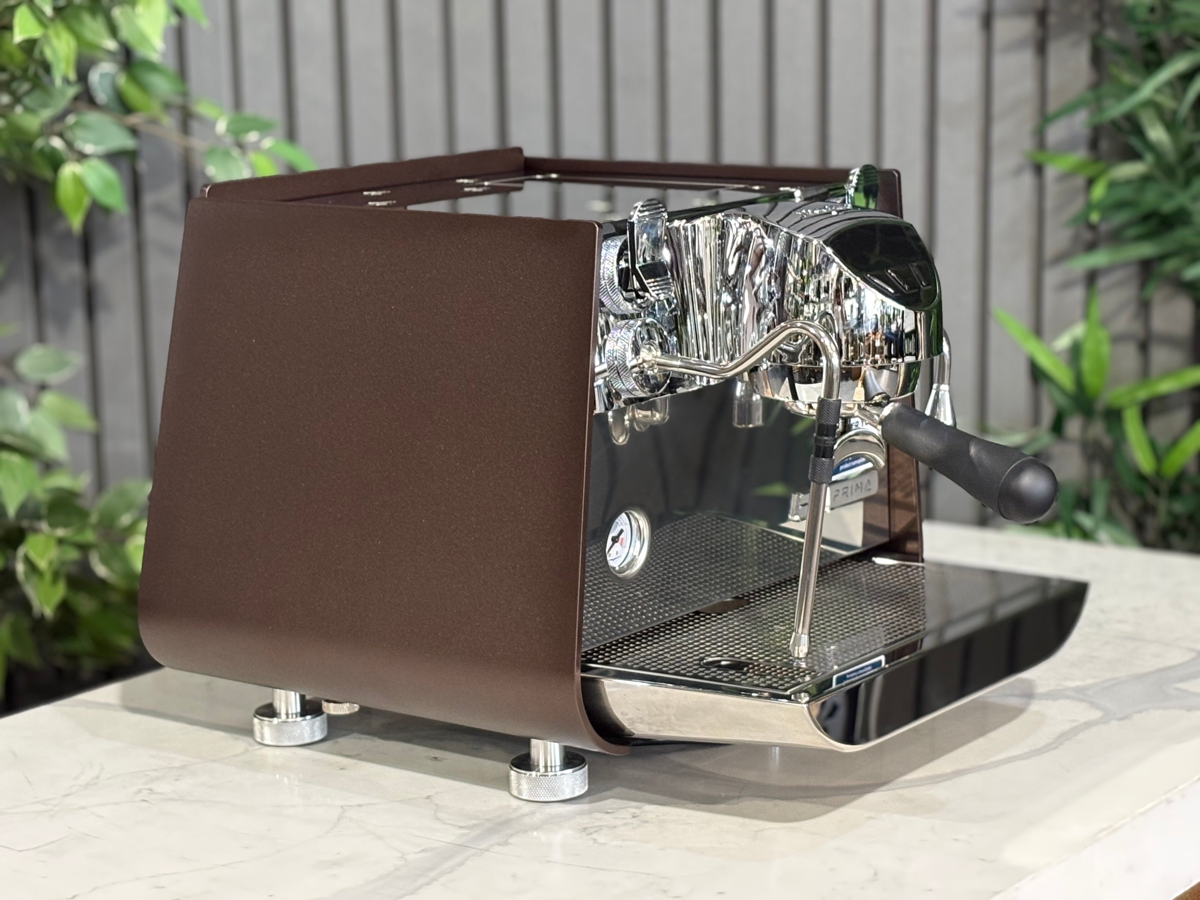 Victoria Arduino Eagle One Prima 1 Group Espresso Machine in burnished copper finish on a table with green foliage.