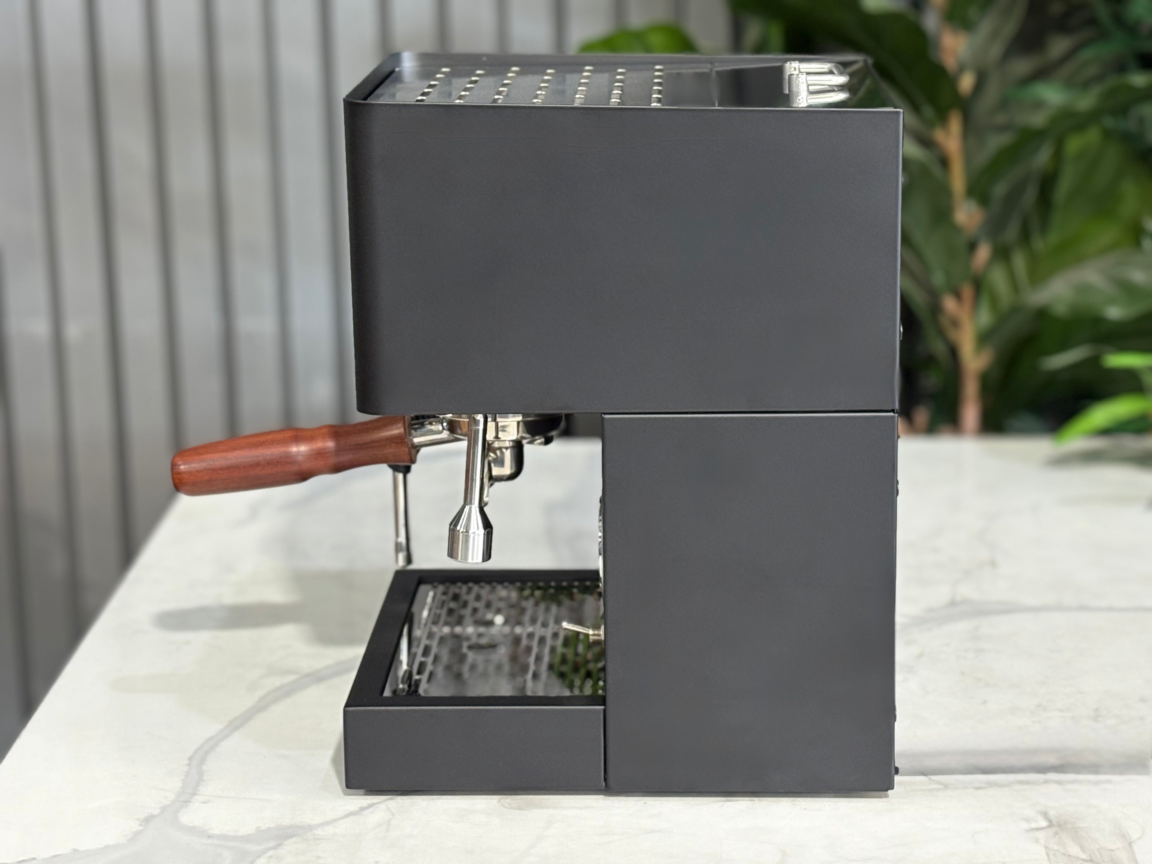 Essenza Nina 1 Group Coffee Machine Stainless side view on a countertop with sleek design and wooden handle.