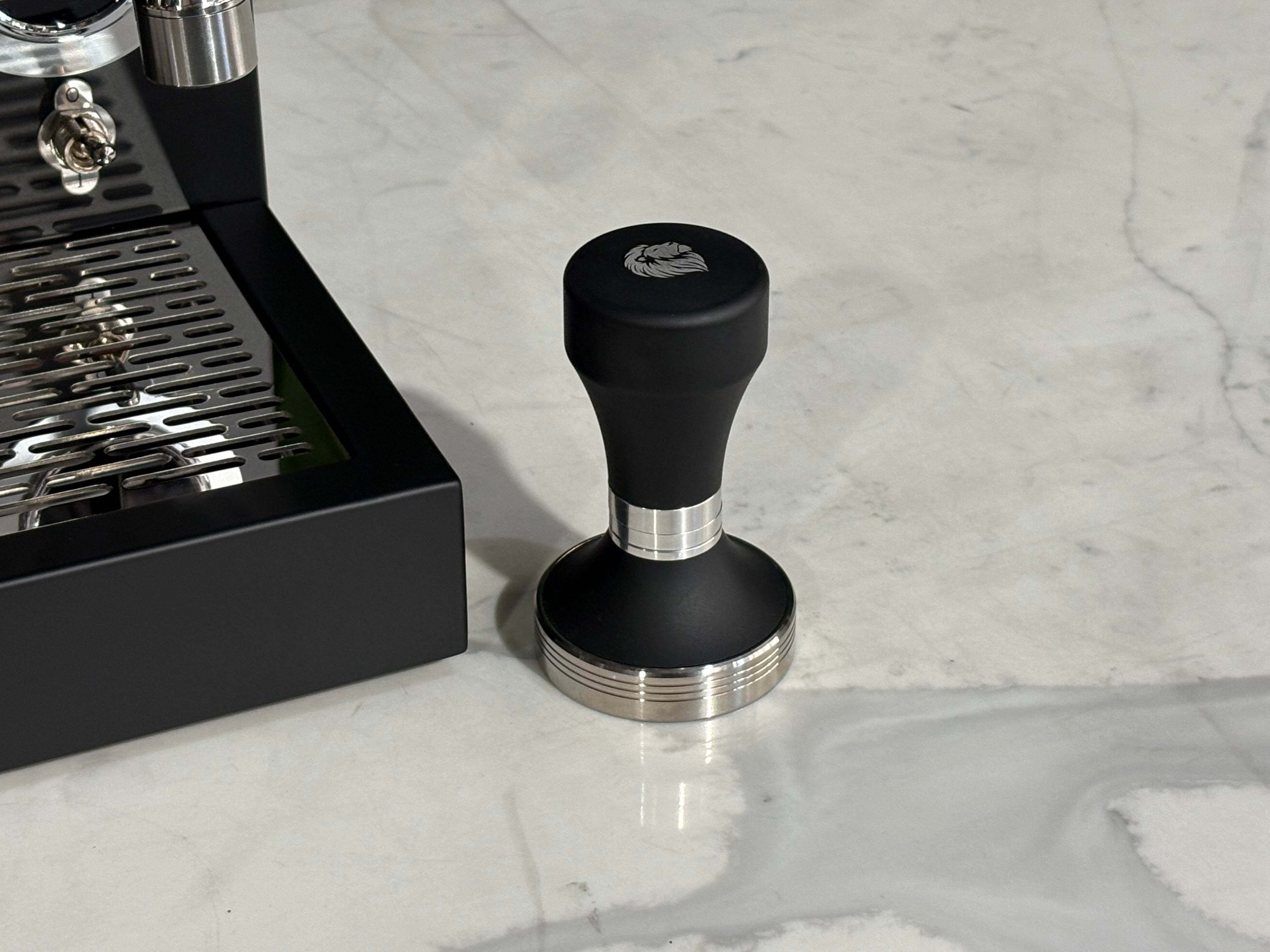 Essenza Nina 1 Group Coffee Machine Stainless tamper on marble surface next to espresso machine.