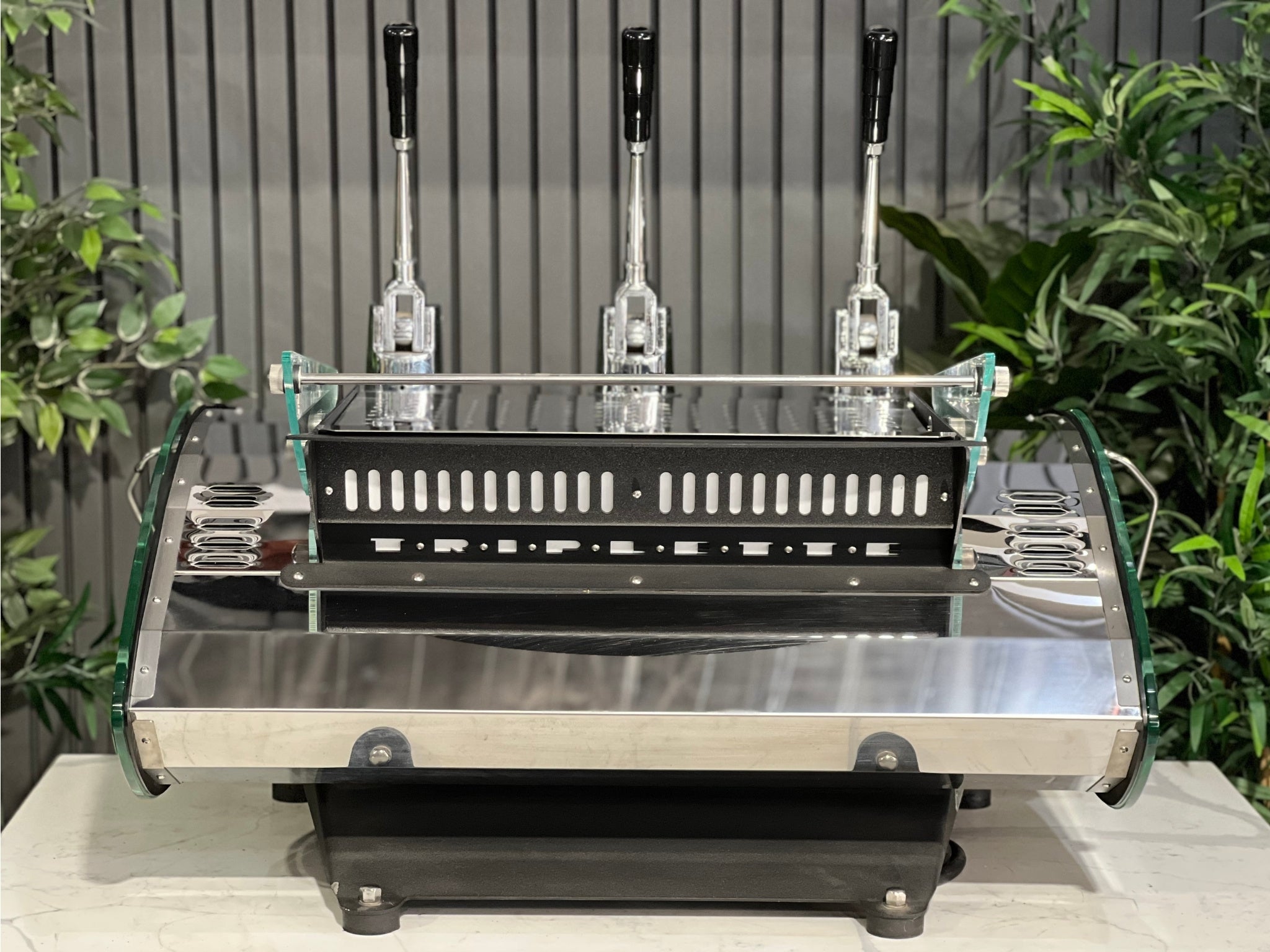 Kees van der Westen Mirage Idrocompresso Triplette 3 Group Coffee Machine Stainless - Used espresso machine captured from the back. Features the clean stainless steel rear panel and outlines of the lever components, with a marble bench and greenery in the background.