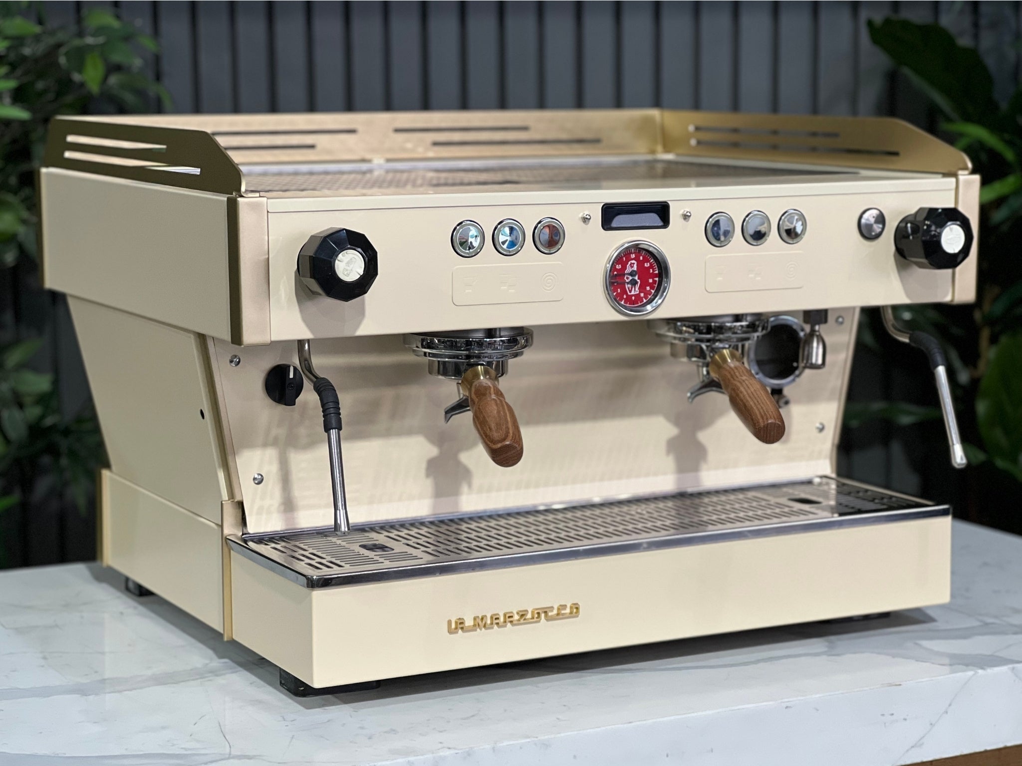 La Marzocco Linea PB 2 Group Coffee Machine Cream & Gold - Used shown at an angle on a marble bench with greenery in the background. This espresso machine features a striking cream and gold body, dual group heads, and digital controls for professional espresso performance.
