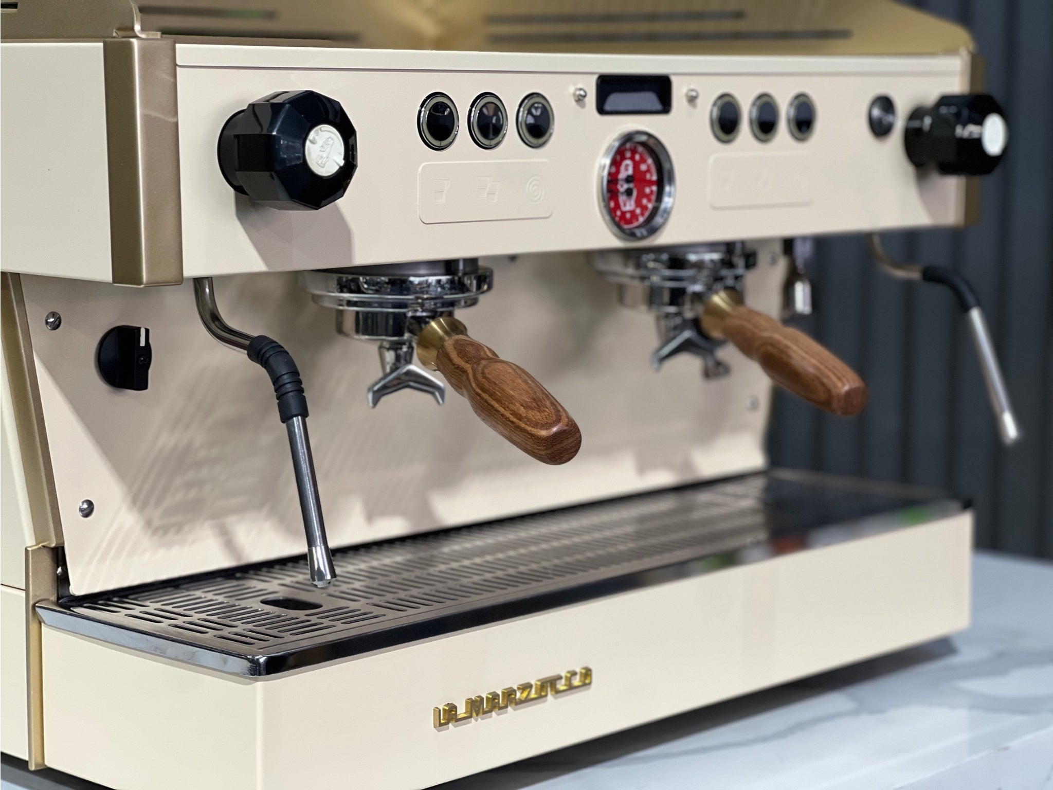 La Marzocco Linea PB 2 Group Coffee Machine Cream & Gold - Used captured close-up from the front on a marble bench with greenery. This espresso machine highlights its programmable buttons, group heads, and user-friendly controls for precision brewing.