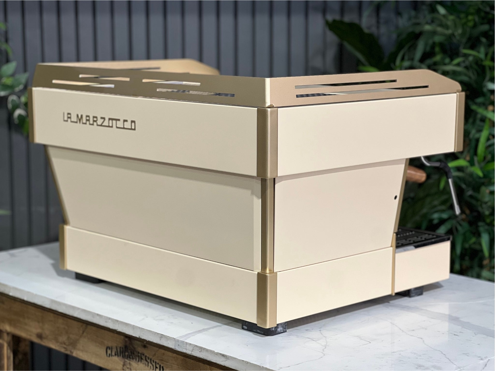 La Marzocco Linea PB 2 Group Coffee Machine Cream & Gold - Used shown at an angled back view on a marble bench with greenery. The espresso machine’s elegant design and premium build are clearly visible from this rear perspective.

