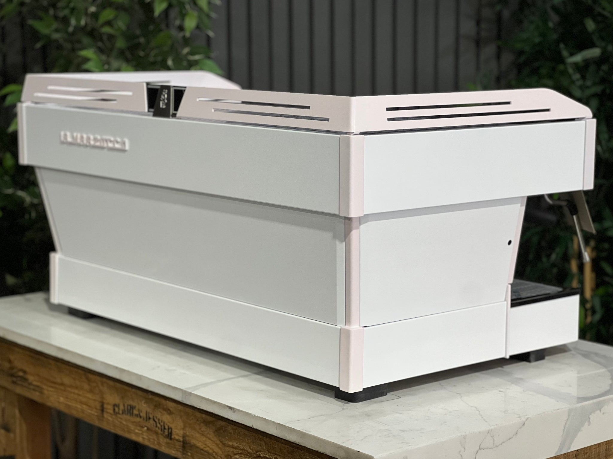 La Marzocco Linea PB 3 Group Coffee Machine White & Pink - New espresso machine angled rear view, highlighting its sleek dual-tone panels and durable stainless steel body, sitting on a marble bench with greenery in the background.