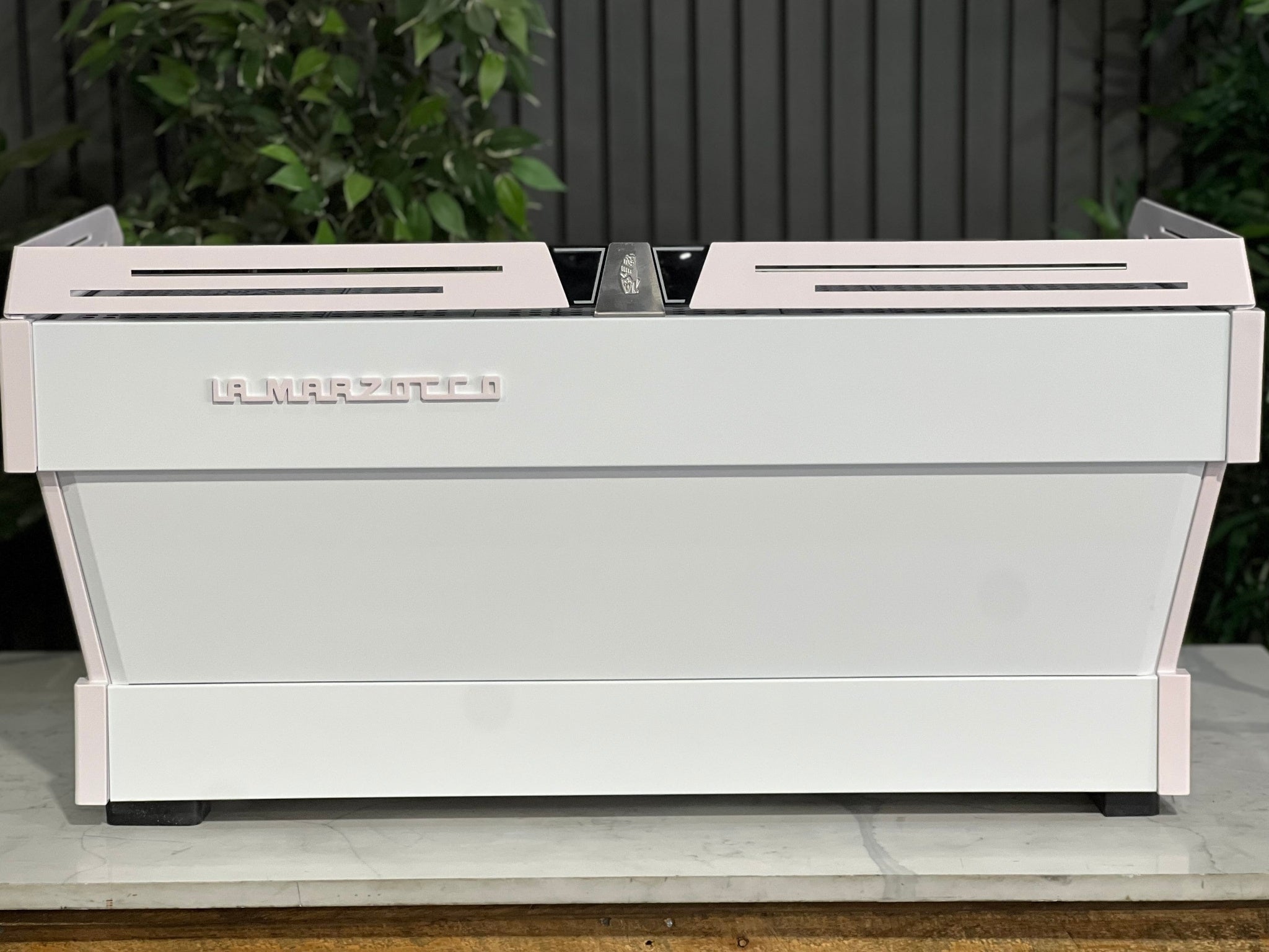 La Marzocco Linea PB 3 Group Coffee Machine White & Pink - New espresso coffee machine rear view, showcasing its custom white and pink body with stainless steel accents, placed on a marble bench with greenery in the background.