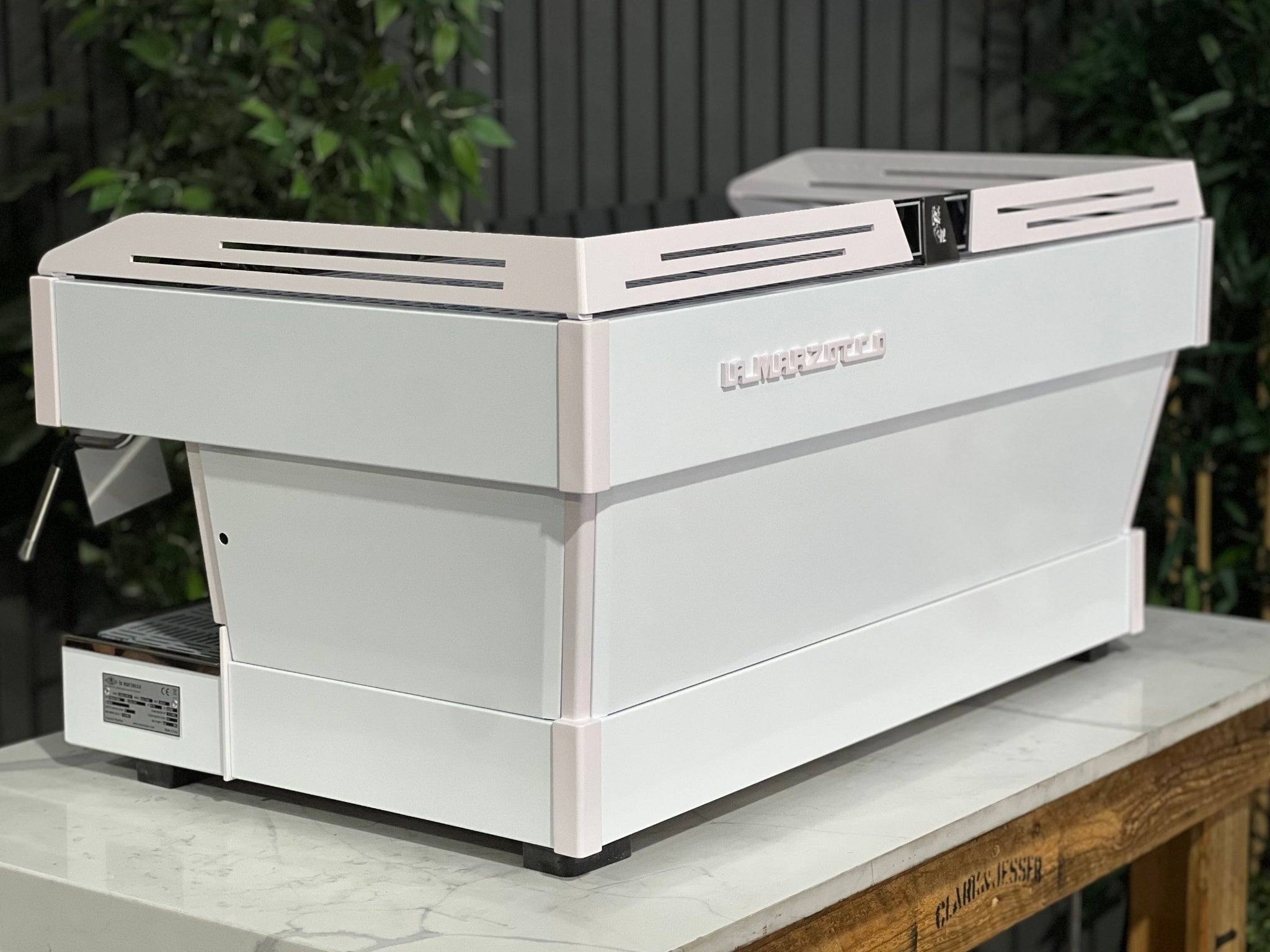 La Marzocco Linea PB 3 Group Coffee Machine White & Pink - New espresso machine angled rear view, highlighting its sleek dual-tone panels and durable stainless steel body, sitting on a marble bench with greenery in the background.
