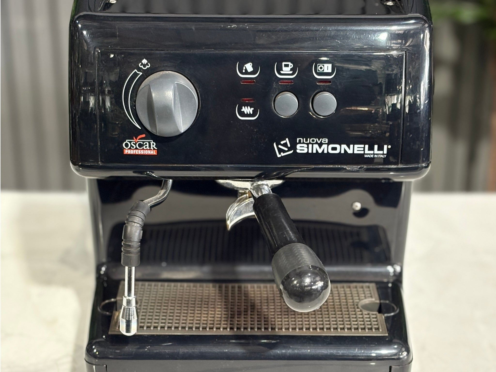 Close-up of the Nuova Simonelli Oscar Professional 1 Group Coffee Machine Black - Used espresso machine, focusing on the group head, steam knob, and cup tray. Captured on a marble bench with greenery behind.