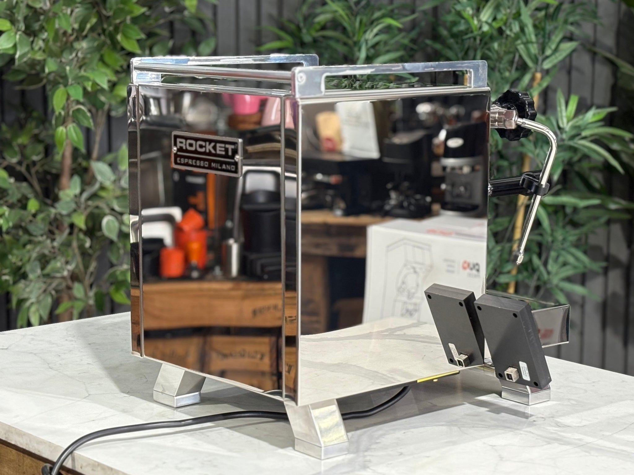 Rocket Cinquantotto R58 1 Group Coffee Machine Stainless - New angled rear view highlighting the stainless steel body, dual boiler outline, water tank access, and overall compact design on a marble bench with greenery backdrop.