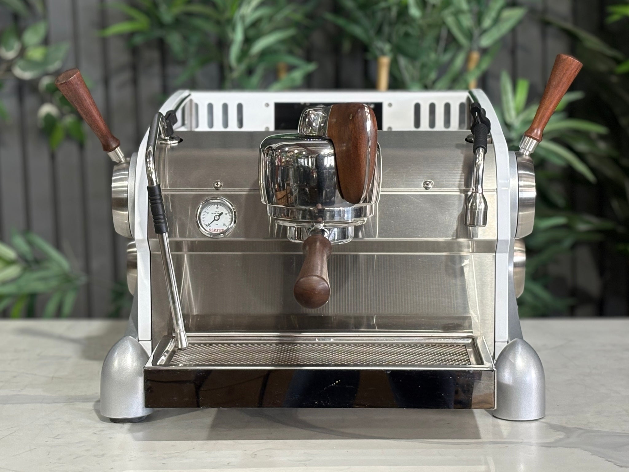 Slayer Espresso 1 Group Coffee Machine White – Used, front-on view showing the single group head, manual paddle control, dual steam wands, and cup tray of the espresso coffee machine, set on a marble bench with greenery behind.