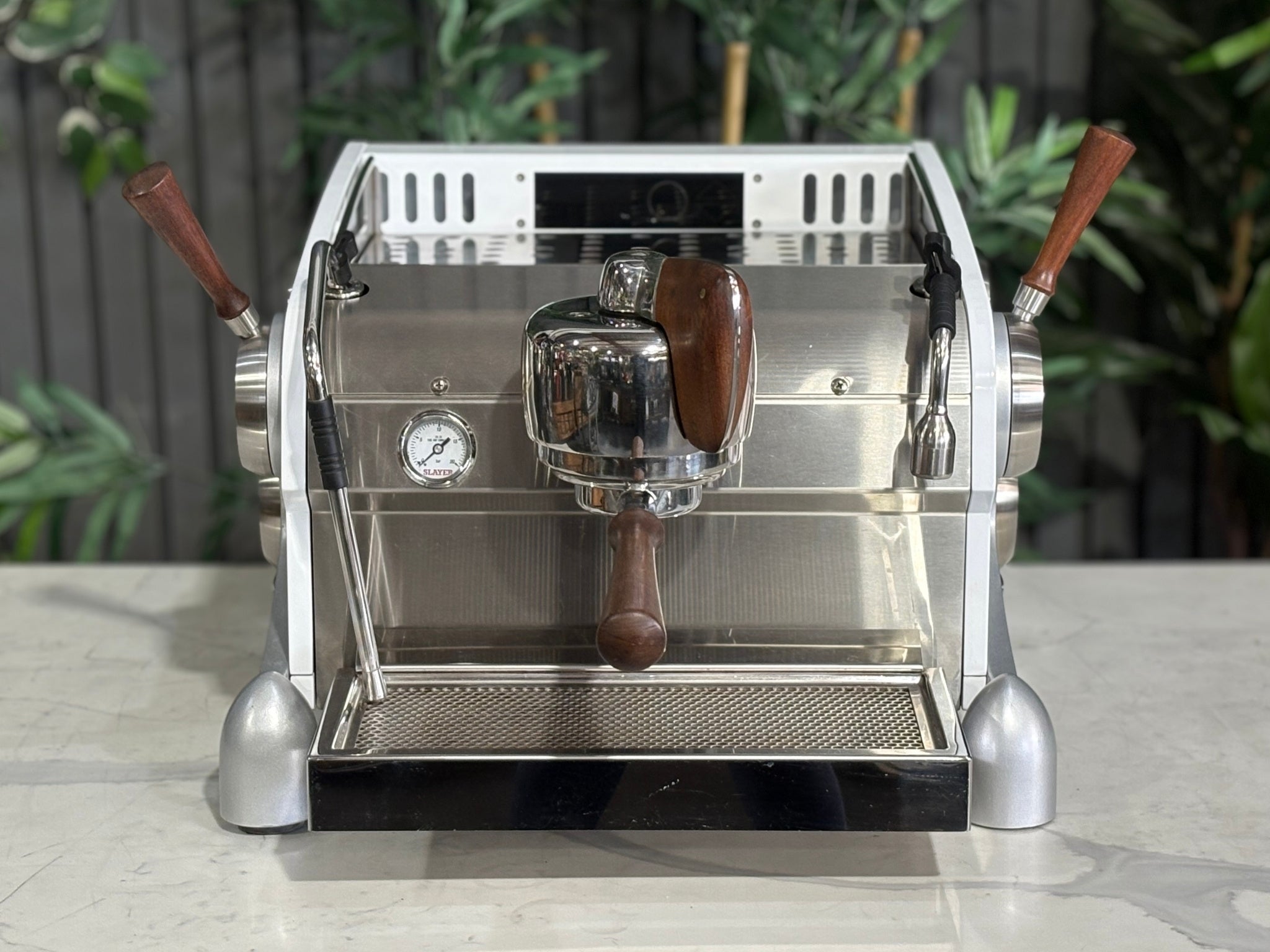 Slayer Espresso 1 Group Coffee Machine White – Used, front view capturing the cup tray and top surface along with the group head, manual paddle, and timber accents of the espresso coffee machine on a marble bench with greenery visible in the background.