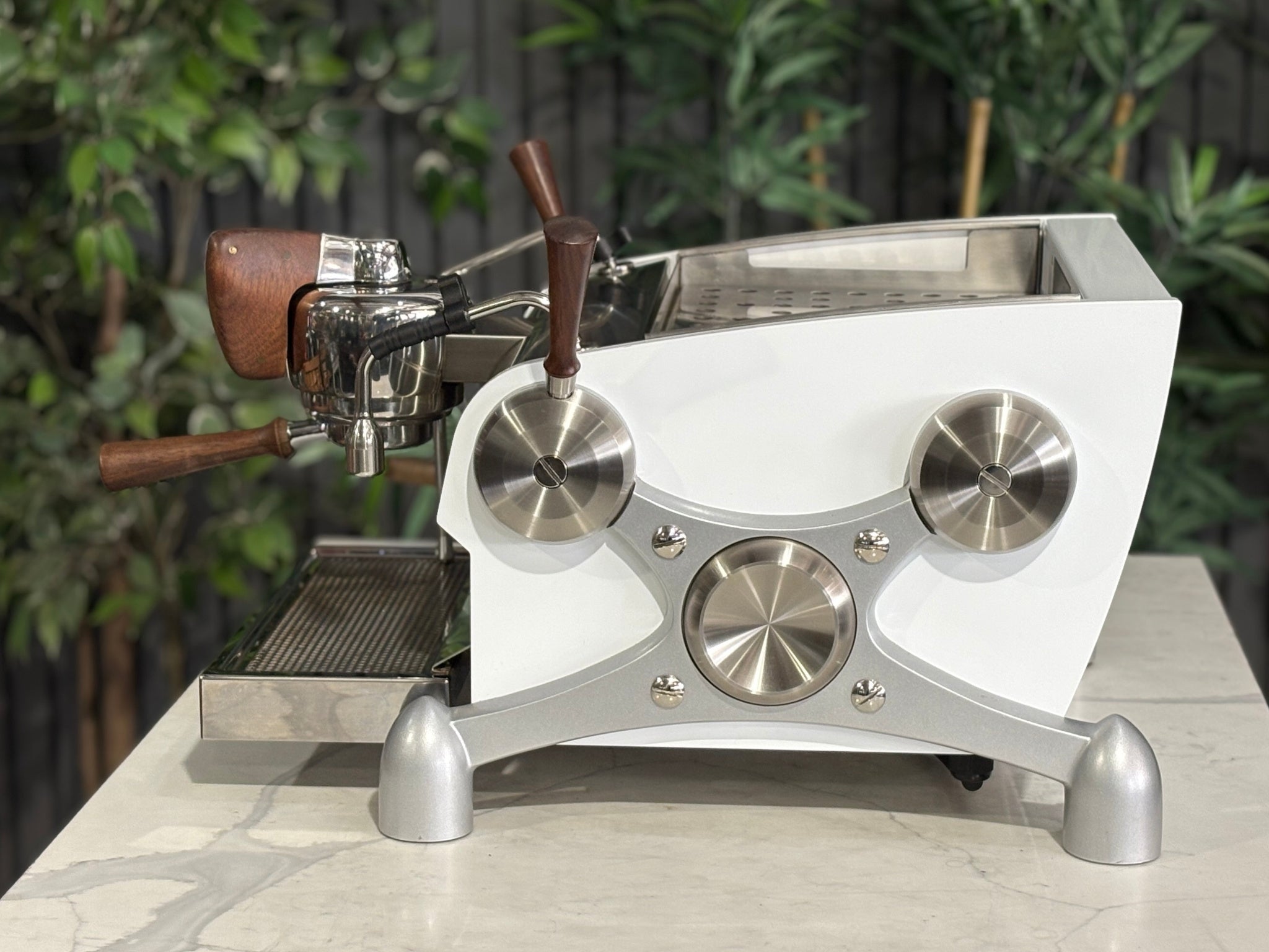 Slayer Espresso 1 Group Coffee Machine White – Used, side profile view highlighting the white body, timber handles, and steam wand detail of the espresso coffee machine on a marble bench with greenery in the background.