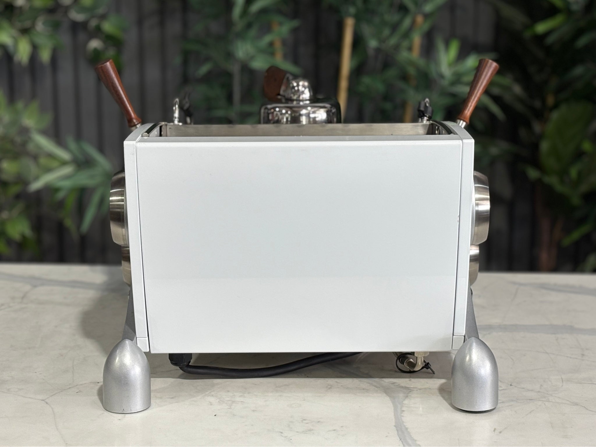 Slayer Espresso 1 Group Coffee Machine White – Used, rear view displaying the smooth white back panel and signature Slayer design of the espresso coffee machine, positioned on a marble bench with greenery behind.