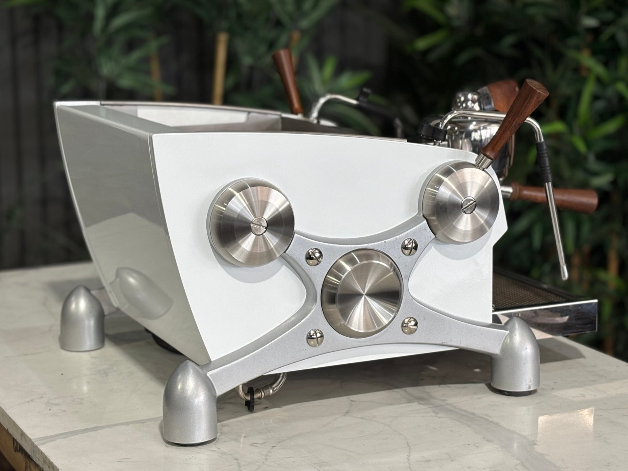 Slayer Espresso 1 Group Coffee Machine White – Used, angled back view showing the rear panel, side profile, and dual steam wands of the espresso coffee machine on a marble bench with greenery visible behind.