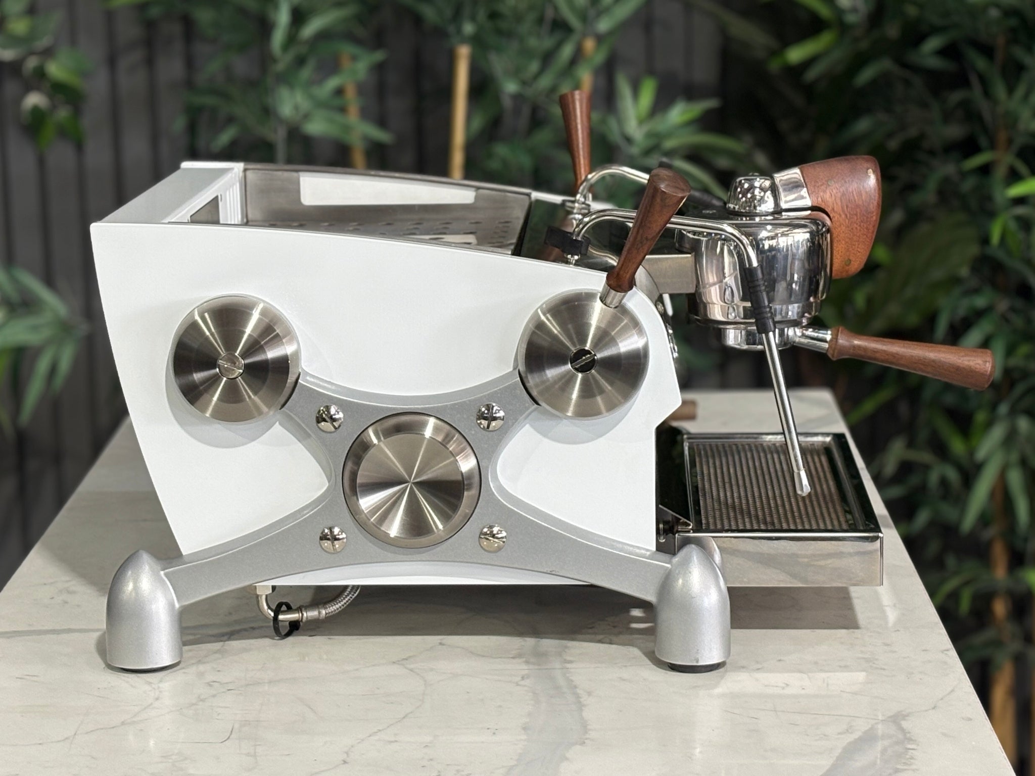 Slayer Espresso 1 Group Coffee Machine White – Used, side profile view highlighting the white body, timber handles, and steam wand detail of the espresso coffee machine on a marble bench with greenery in the background.